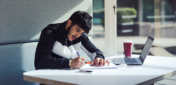 Shot of a student sat in a booth in Student Central. He is studying and using his laptop.