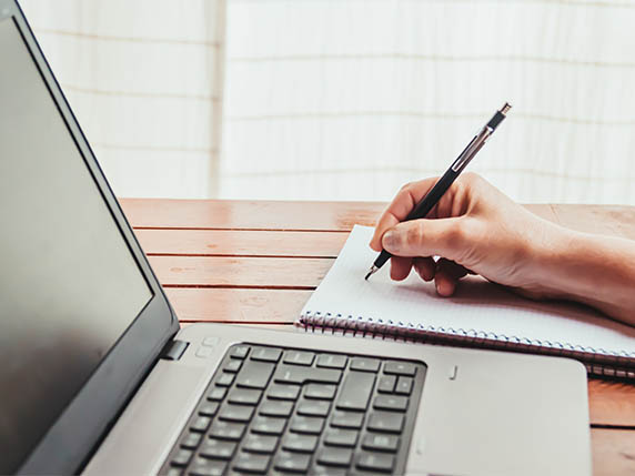 hand making notes in front of laptop