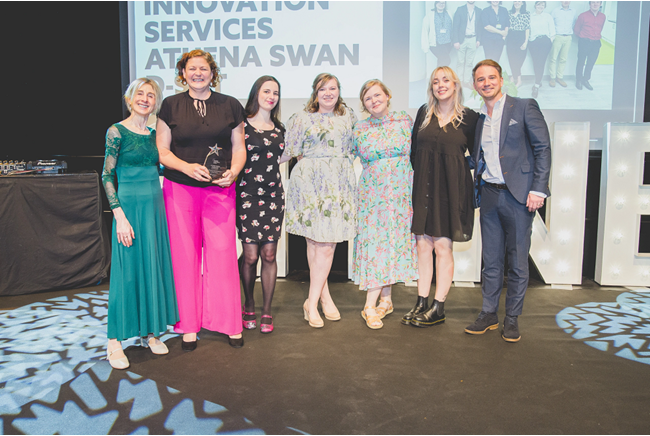 A group of people stood arm in arm in front of a screen holding an award