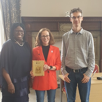 Three people stood smiling, one holding up a book
