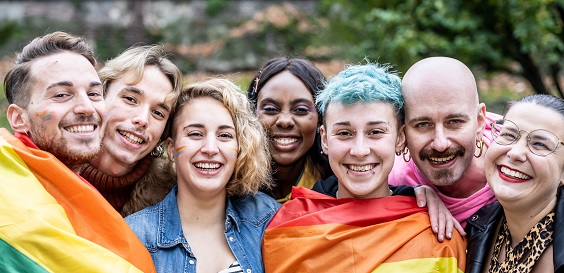 A group of people smiling, two wrapping a PRIDE flag around them 