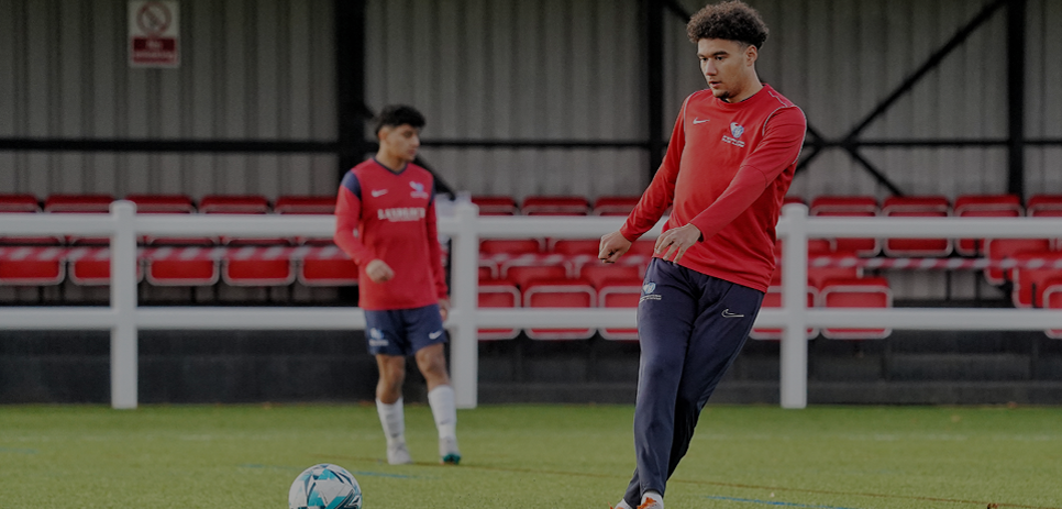Two male student-athletes training at Northumbria University Coah Lane Training Grounds. One of the student-athletes is about to kick a soccer ball.
