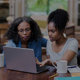 Mother and daughter sitting at a table and working on a laptop.