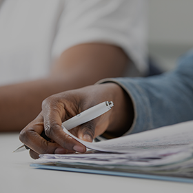 Close-up of a student writing in a file with a Northumbria University branded pen.