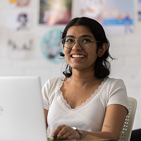 Design student sat in front of a laptop, smiling.