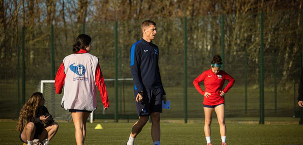 Coach with female i2i students on pitch