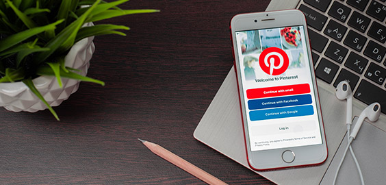 Pinterest on mobile phone sat on computer with pencil plant and headphones