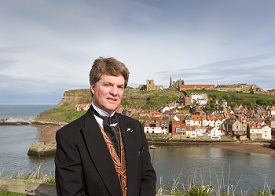 a man wearing a suit and tie standing next to a body of water