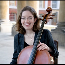 lady with brown hair and glasses sat in an old building holding a cello