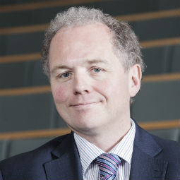 a man wearing a suit and tie smiling at the camera