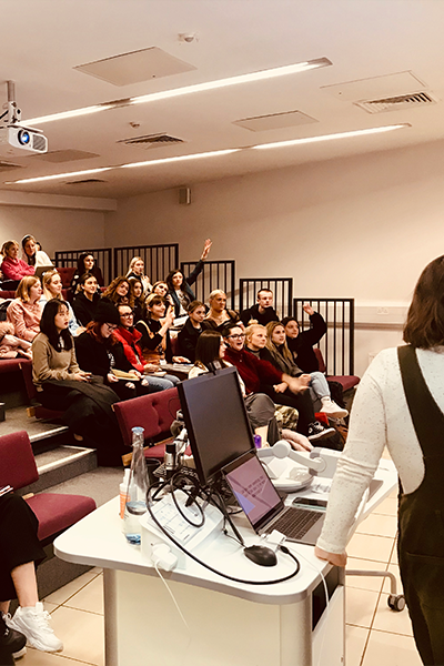 Tiered lecture theatre filled with students raising their hands.