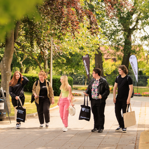 A group of students walking along a path. There are leafy trees in the background.