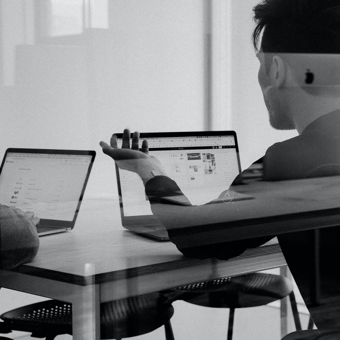 Black and white image of a man working on laptop at a computer desk. 