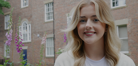 Blonde student in a white tshirt standing in front of house smiling