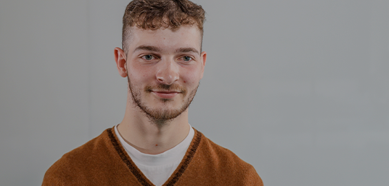 Student wearing white shirt and brown jumper smiling