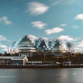a large ship in a body of water with Sage Gateshead in the background