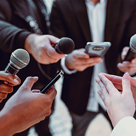 Reporters with microphones and phones interviewing someone