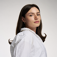 Girl with brown hair, wearing white top, smiling at camera
